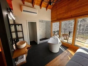 Modern bathroom with freestanding tub, wood ceiling beams, and large windows