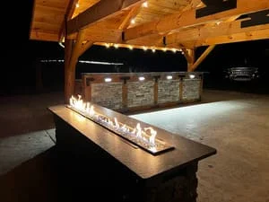Timber pavilion with linear fire pit, wooden beams, and recessed lighting at night
