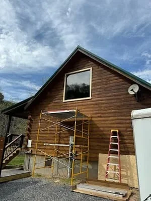 Wood siding installation on cabin with large gable window and temporary scaffolding