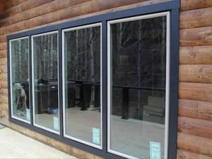 Four-panel sliding glass doors with dark aluminum frames installed on log cabin exterior