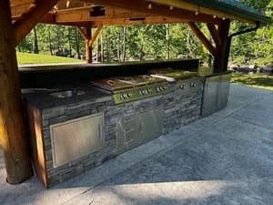 Stainless steel outdoor kitchen with built-in grill and cabinetry under timber pavilion