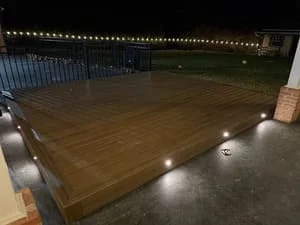 Stained concrete patio with perimeter landscape lighting and aluminum fence at dusk