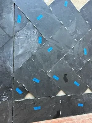 Slate tile installation with blue tape markers showing grout joint layout and diagonal pattern placement