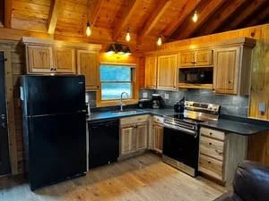 Cabin kitchen with wood cabinetry, exposed beams, granite counters, and black appliances