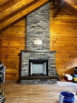 Stacked slate stone fireplace with insert in log cabin interior with exposed wood beams