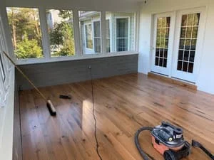 Hardwood floor refinishing in progress with sanding equipment and natural wood flooring visible