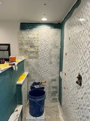 Bathroom with geometric tile shower walls, teal vanity cabinet, and recessed lighting