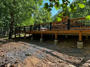 Elevated composite deck with railings on concrete pilings, surrounded by trees
