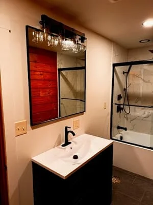 Modern bathroom with black vanity, white sink, framed mirror, and glass shower enclosure