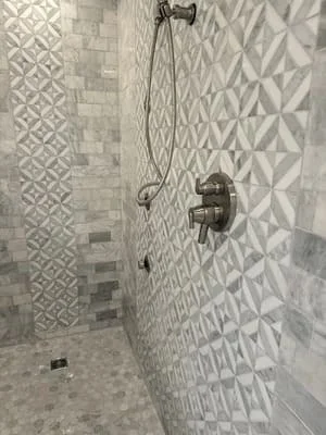 Tiled shower enclosure with geometric wall patterns and mosaic floor tile