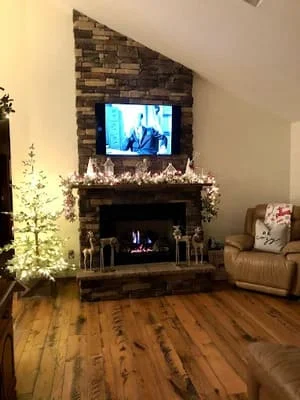 Stacked stone fireplace wall with mounted TV, hardwood floors, and decorative mantel styling