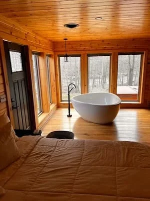 Log cabin bathroom with freestanding tub, wood flooring, and large windows