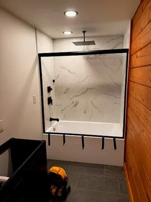 Frameless glass shower with marble tile walls and black hardware in renovated bathroom