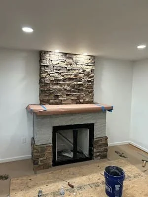 Stacked stone fireplace surround with wood mantel and recessed lighting